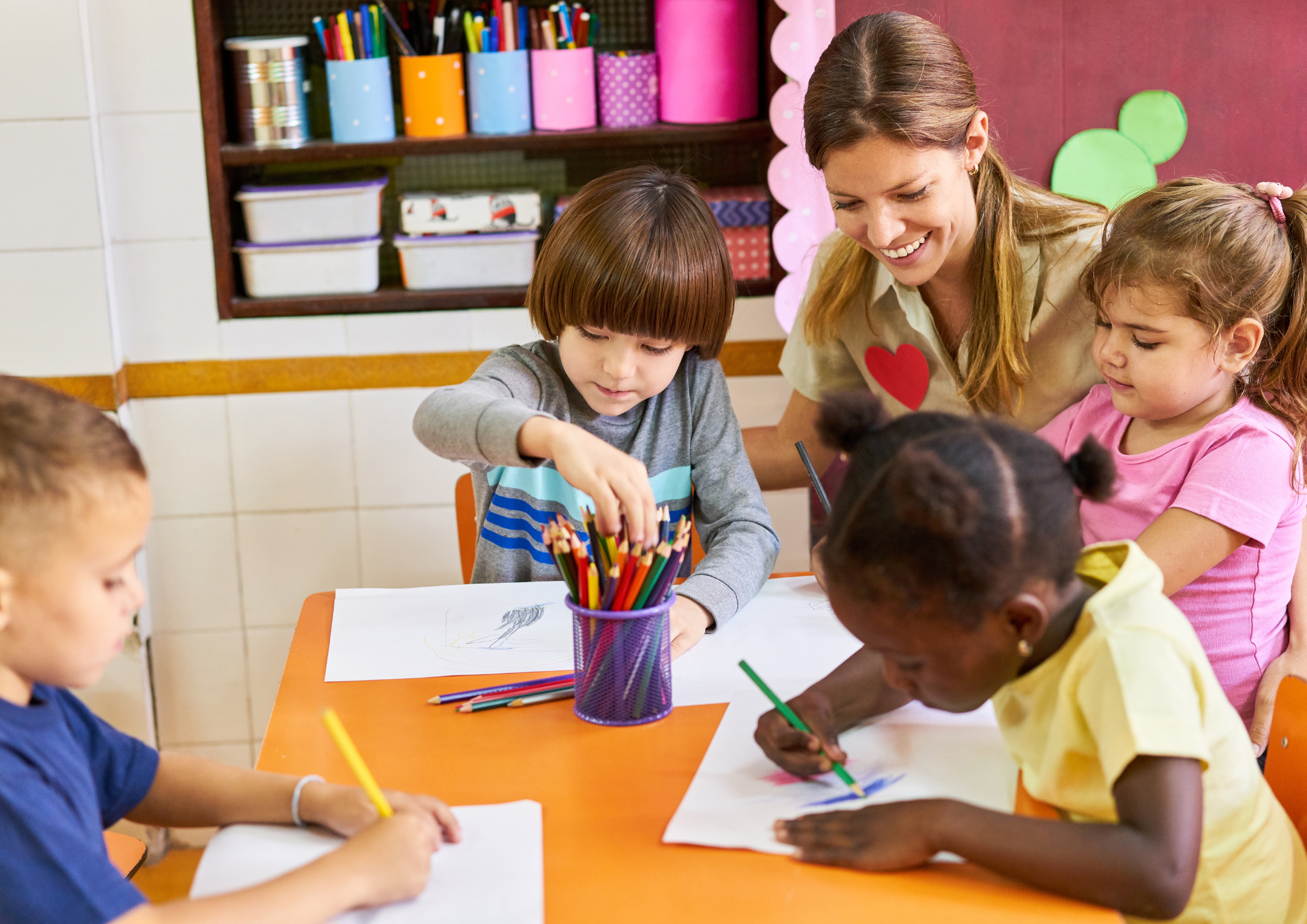 Erzieherin mit malenden Kindern am Tisch. 